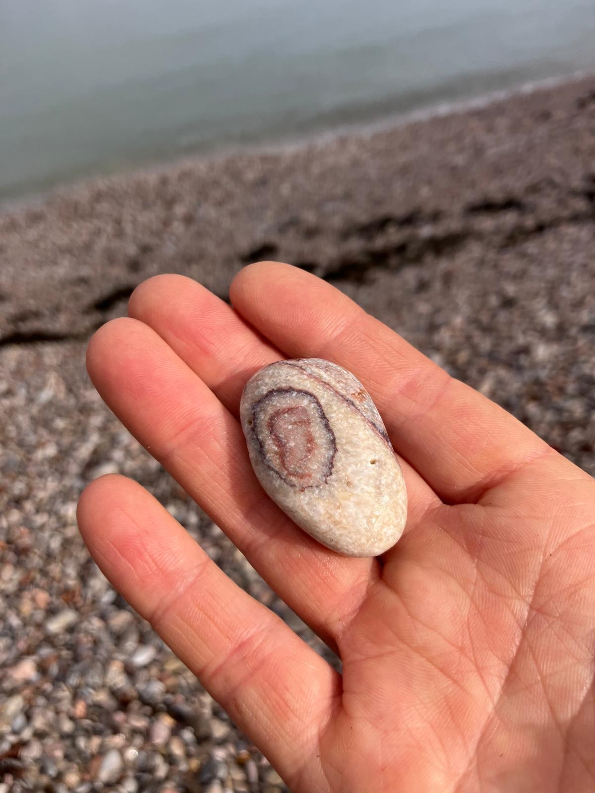 A banded pebble resting in an open hand on a shingle beach